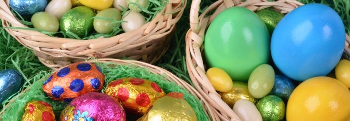 Drei Osterkörbchen gefüllt mit bunten Ostereiern und Süßigkeiten.